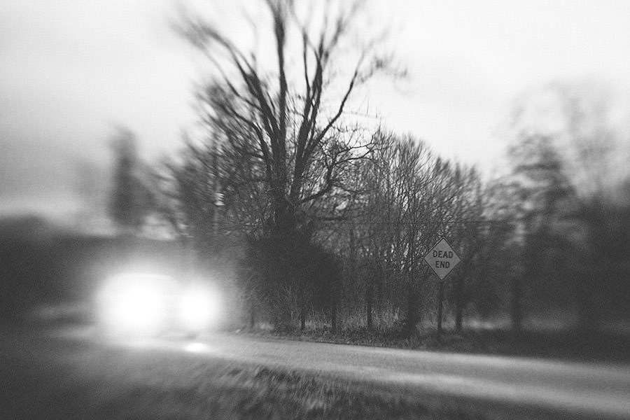 A foggy road at night with oncoming headlights and a Dead End sign